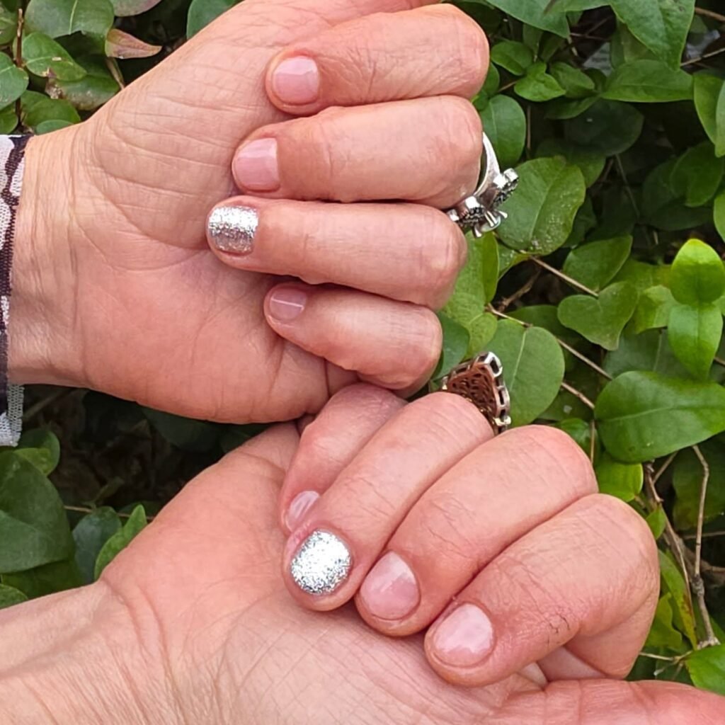 Sparkling silver glitter gel nail ideas for short nails on natural base with rings and green foliage backdrop.