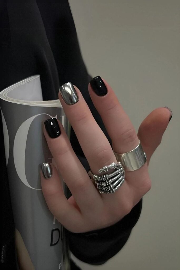 Hand holding a magazine, featuring chrome silver and black nails accessorized with rings, a bold example of short black nails ideas enhanced by metallic elements.