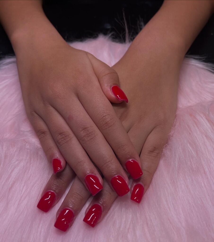 Short red nails ideas highlighted by hands displaying square-shaped nails in a uniform bright red glossy finish.