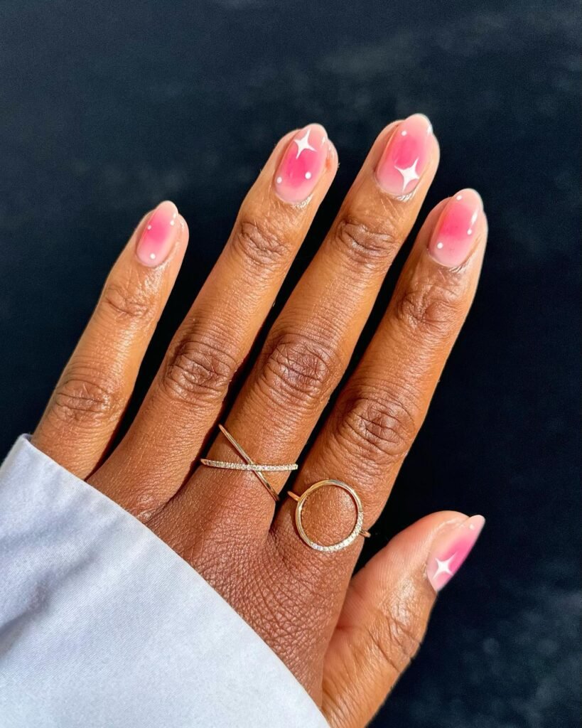 Find cute short almond nails ideas with a gentle pink ombre gradient fading from light base to vivid tips, accented by small white stars and dots for a playful and sparkling manicure that's ideal for adding a touch of whimsy to your look.