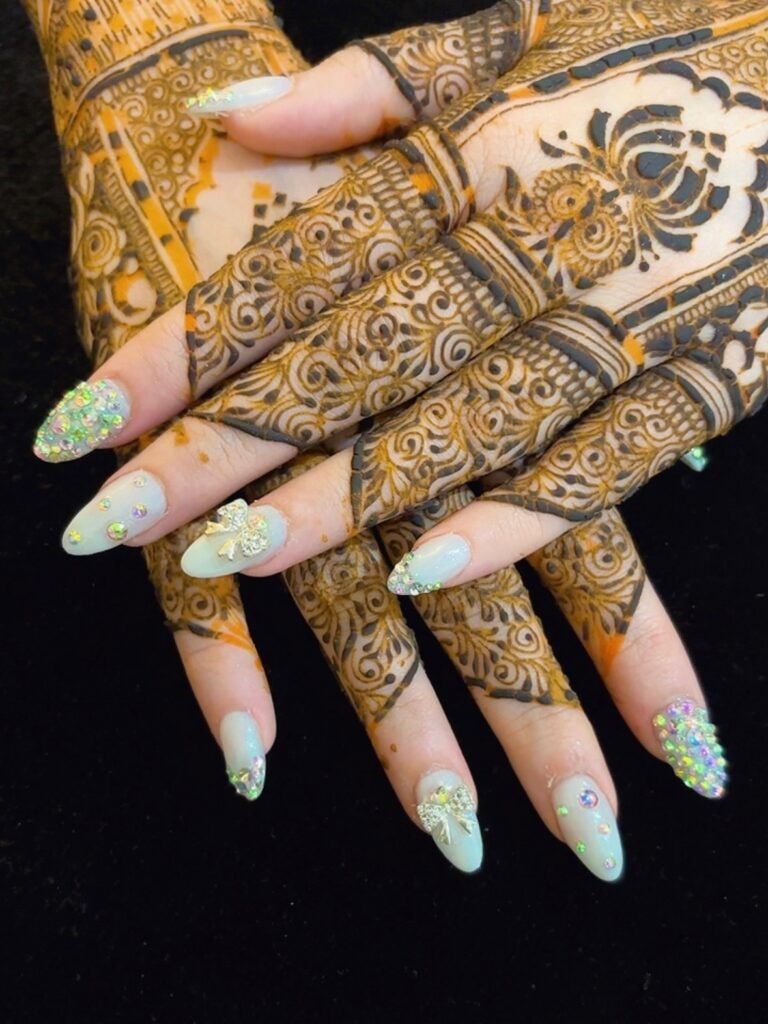 Elegant anniversary nails ideas featuring mint green polish with rhinestones and bow accents paired with traditional henna designs.