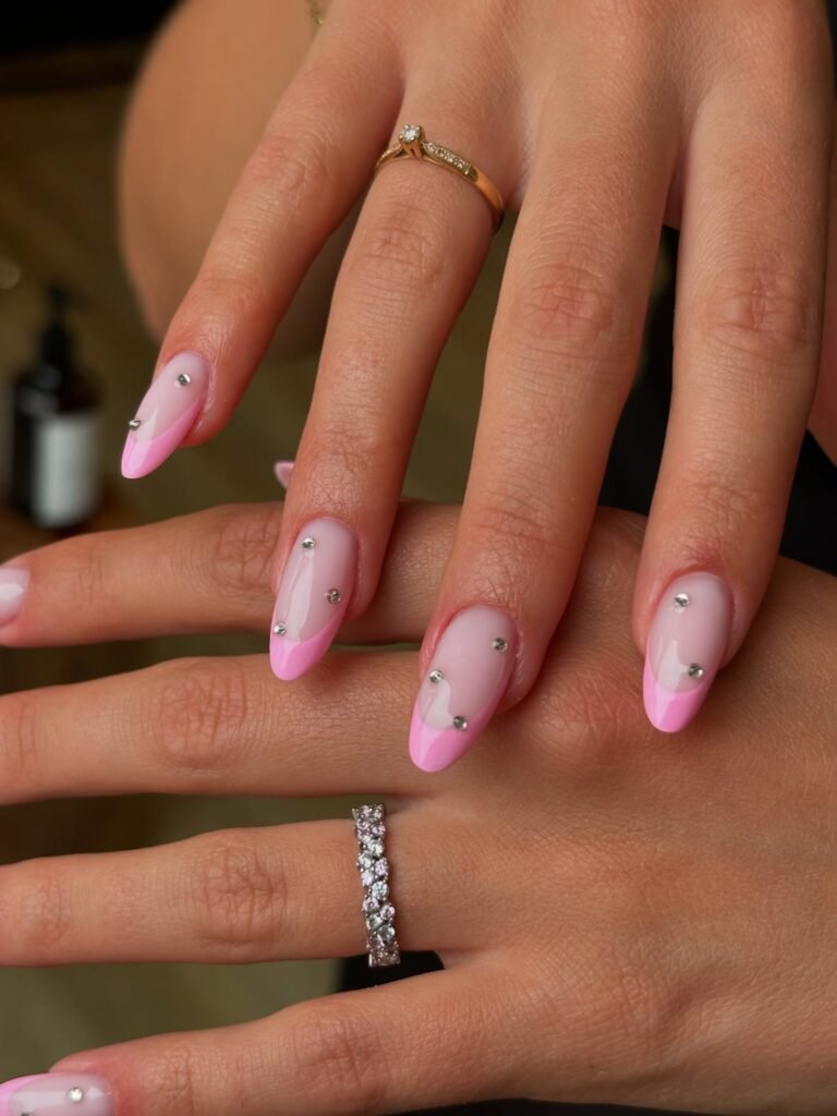 Sparkling barbie nails featuring pink French tips embellished with rhinestones, captured on jeweled hands.