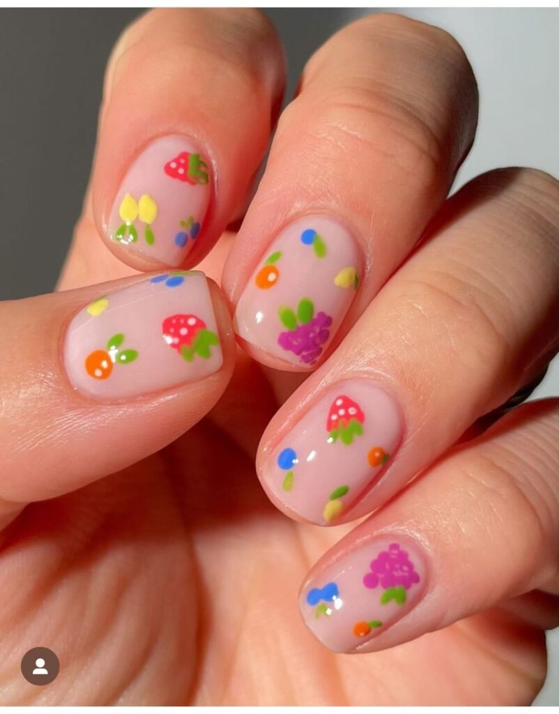 Short spring nails ideas with a milky pink base and tiny colorful fruit nail art including strawberries, grapes, and citrus on short rounded nails.