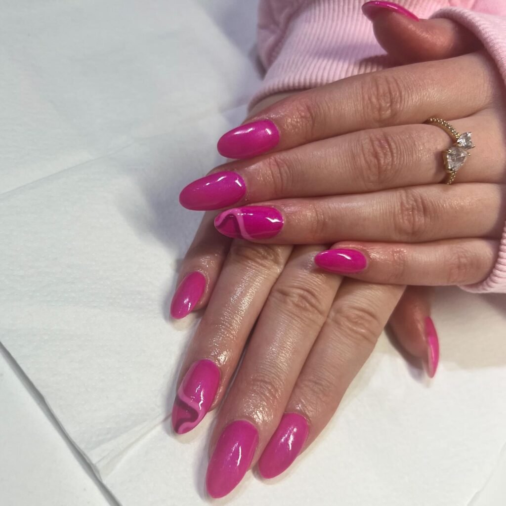 Vibrant pink barbie nails with white swirl accents on select fingers, displayed on hands in a soft pink sweater.