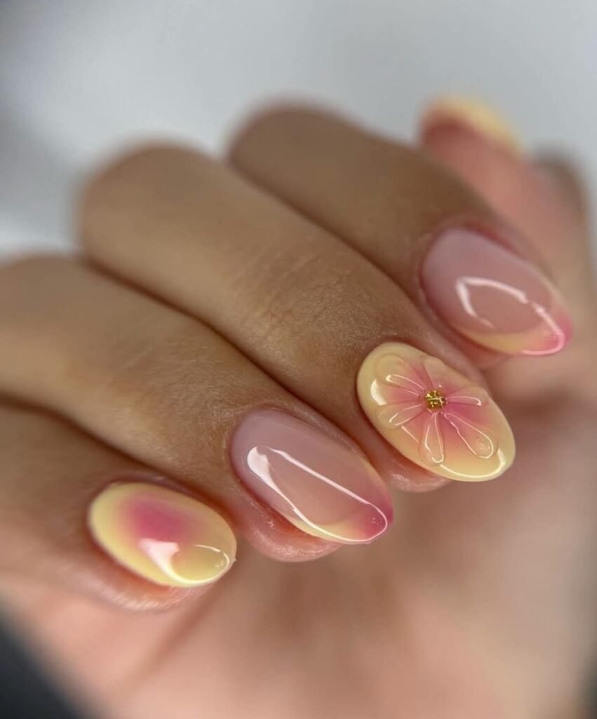 Short spring nails ideas with pink and yellow ombre polish and a delicate floral accent design on glossy short oval nails.