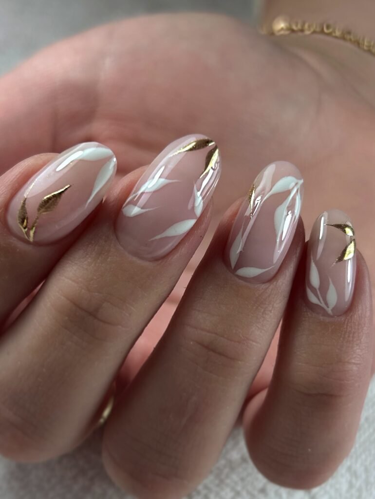 Chic anniversary nails ideas in nude pink with white leaf patterns and gold foil accents for a sophisticated look.
