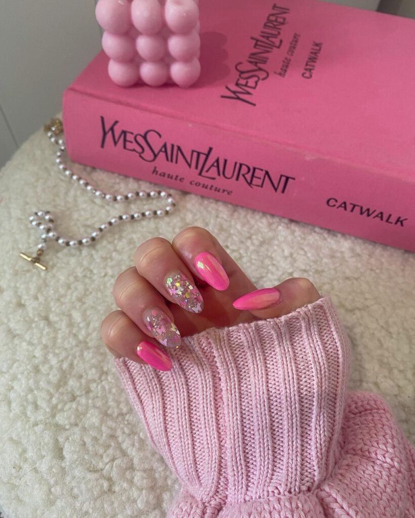 Shimmery barbie nails with pink ombre and glitter confetti details, posed next to fashion accessories.