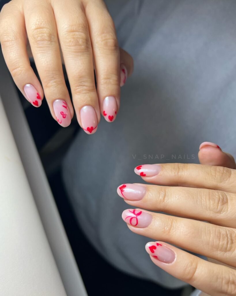 Romantic anniversary nails ideas with light pink base and red heart and ribbon motifs for a loving touch.