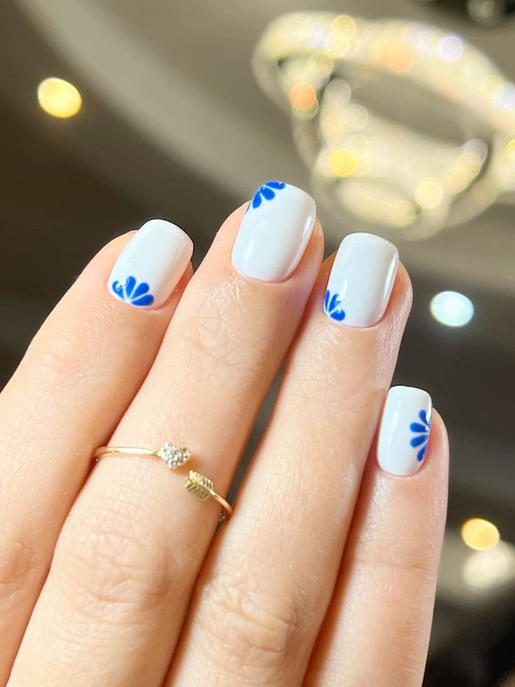 Chic white short nails ideas showcasing blue petal motifs for a minimalist yet striking manicure.