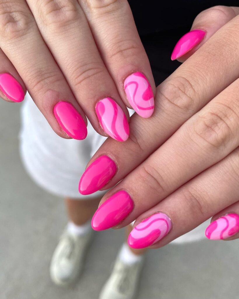 Close-up of vibrant barbie nails with pink and white swirl patterns on almond-shaped tips.