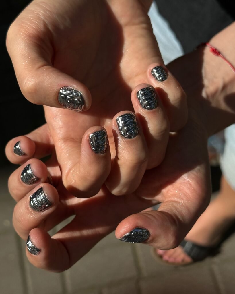 Hands showing simple short nail ideas with a textured silver foil effect for a modern, metallic shine.