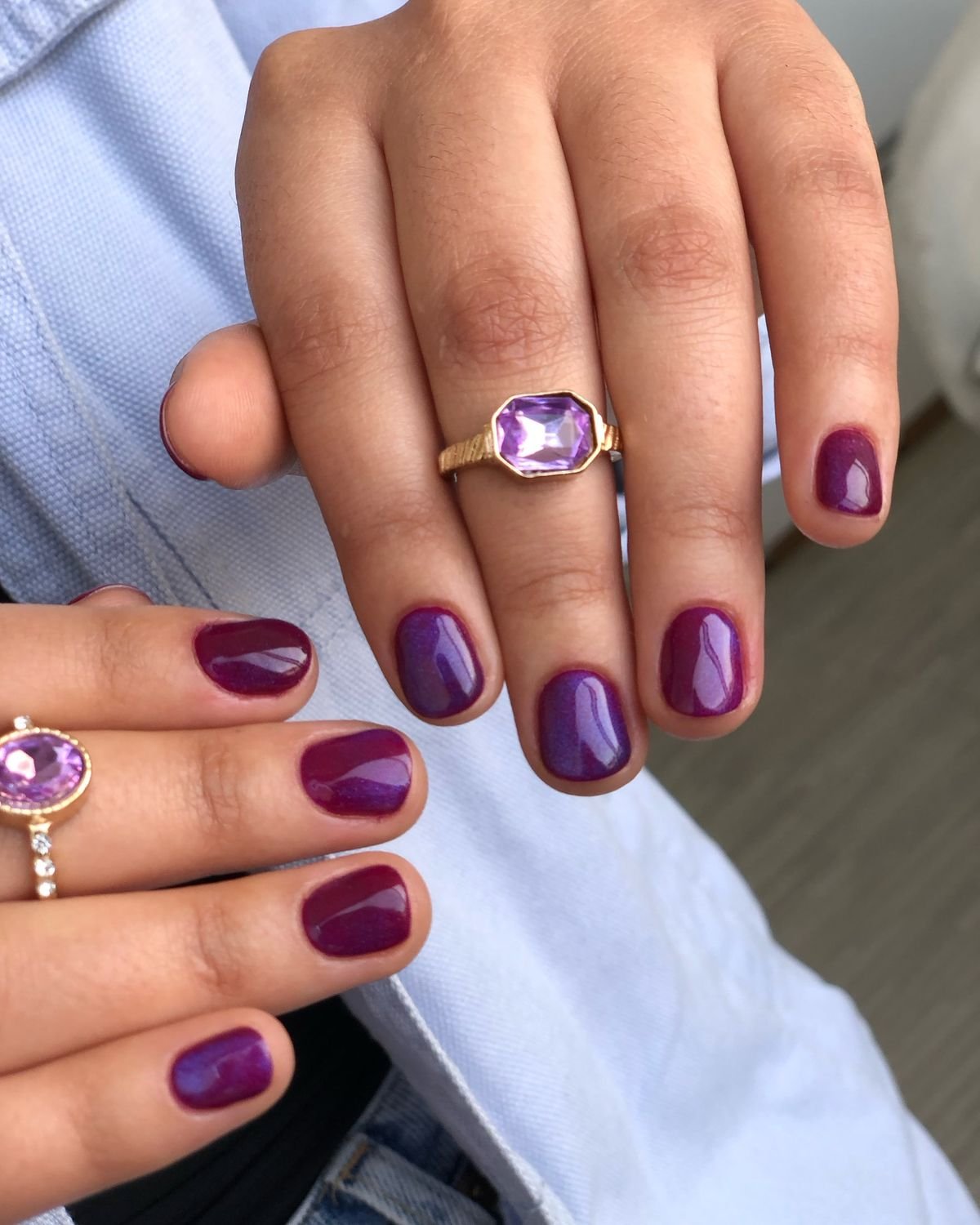 Hand featuring short round nails ideas with deep plum glossy nail polish, vintage rings, and a light blue shirt backdrop for a chic, timeless manicure look