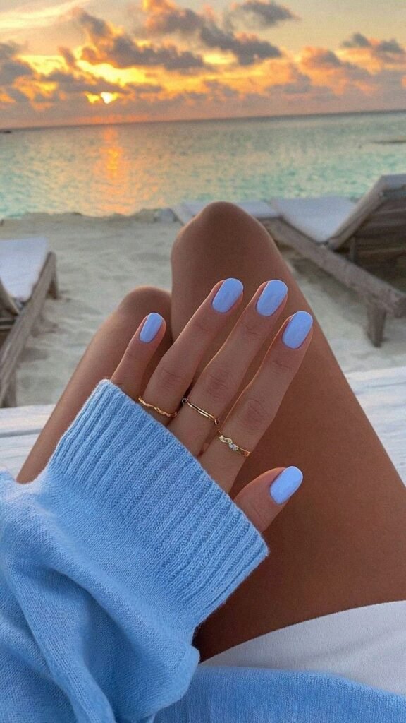 Serene light blue nails against a sunset beach backdrop as short nail ideas for summer getaways.