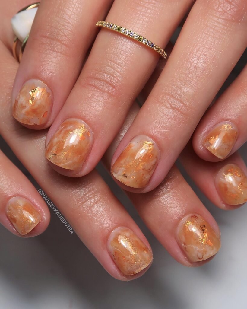Very short nails ideas mimicking orange marble with gold flakes.