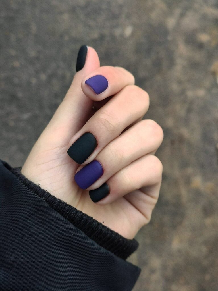 A single hand with matte short nails in black, green, and purple hues, representing versatile short black nails ideas with a subtle color gradient.