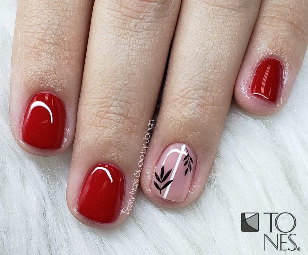 Short red nails ideas featuring predominantly red polish with one pale pink accent nail adorned by black line art of leaves and a stripe.