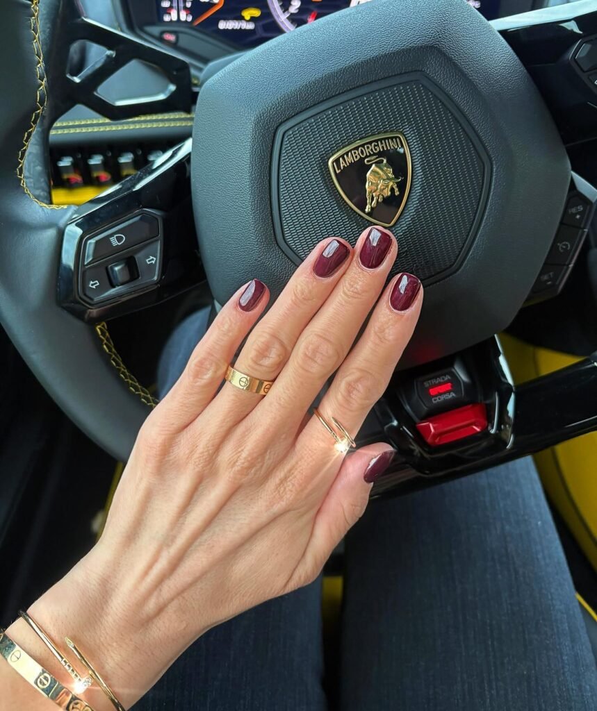 Elegant simple short nail ideas in deep burgundy, captured while holding a Lamborghini steering wheel.