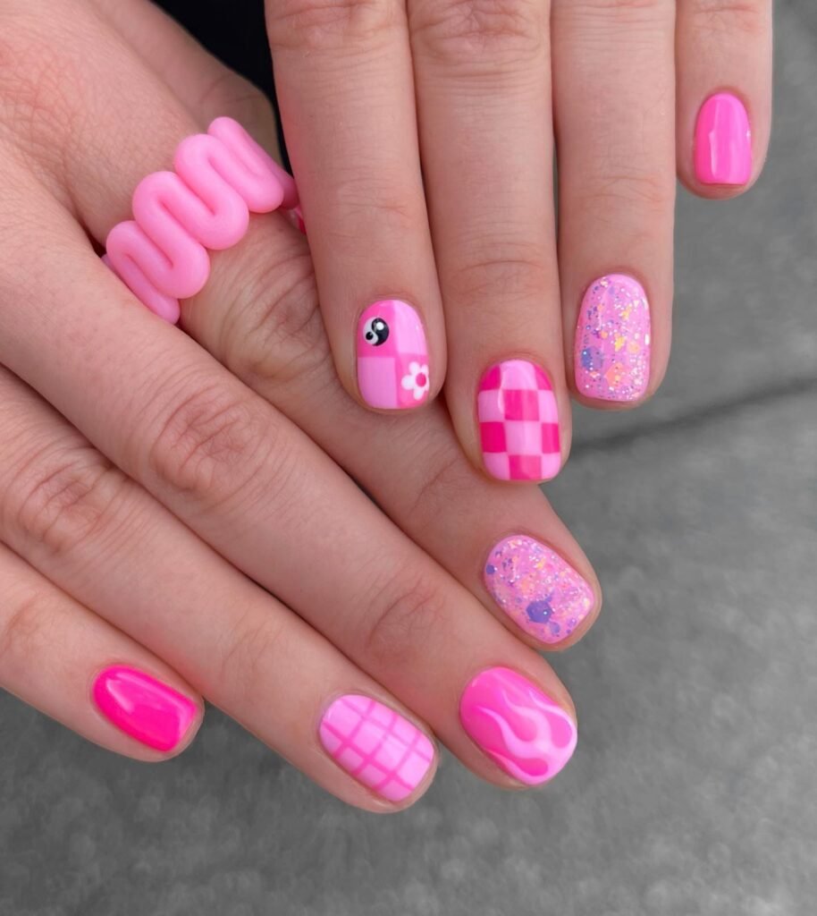 Fun barbie nails featuring a mix of pink designs like yin-yang, checkered patterns, glitter, and flames for a playful look.