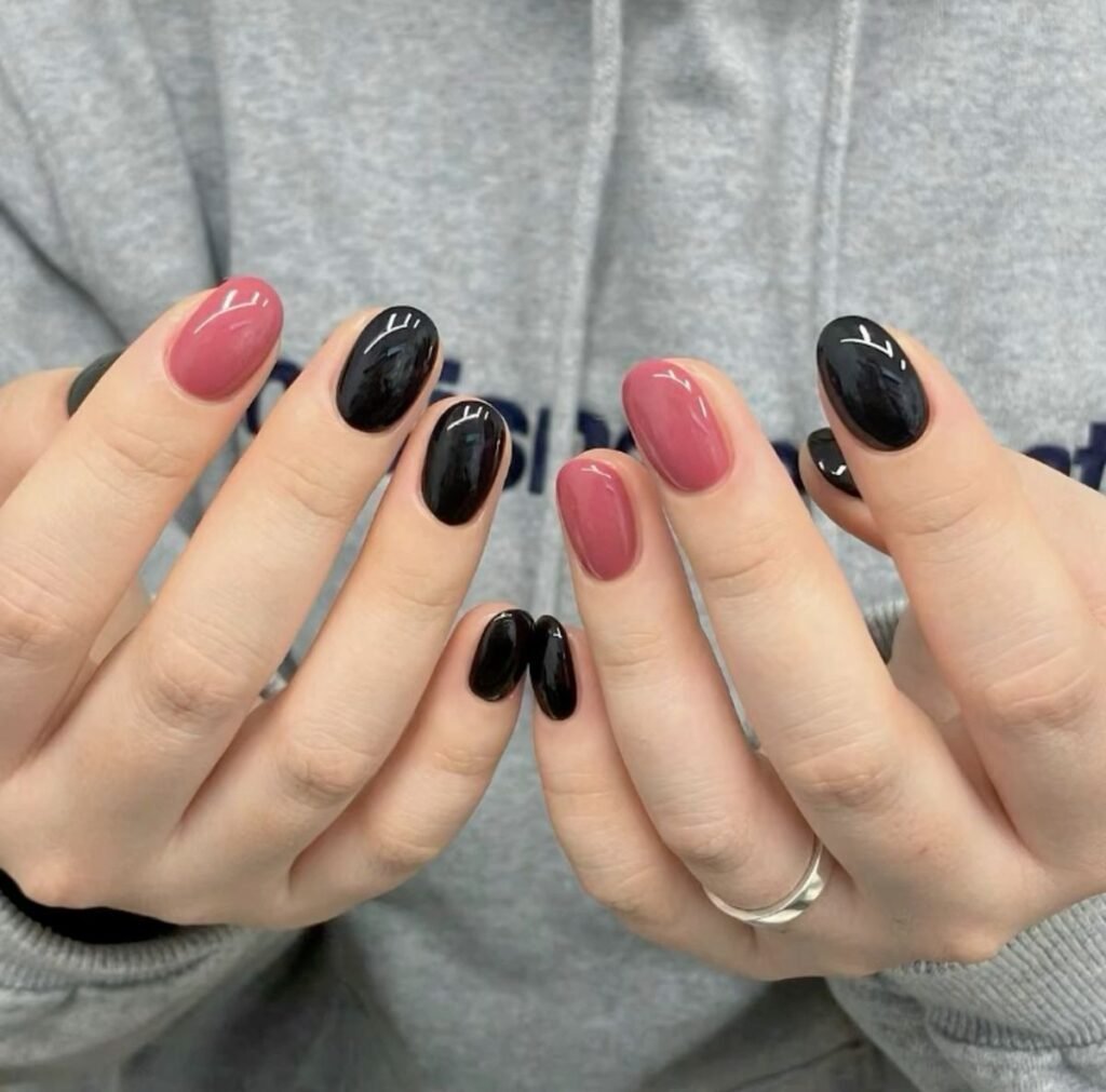 Close-up of hands showcasing alternating glossy black and pink nails, a fresh take on short black nails ideas for a balanced, feminine vibe.