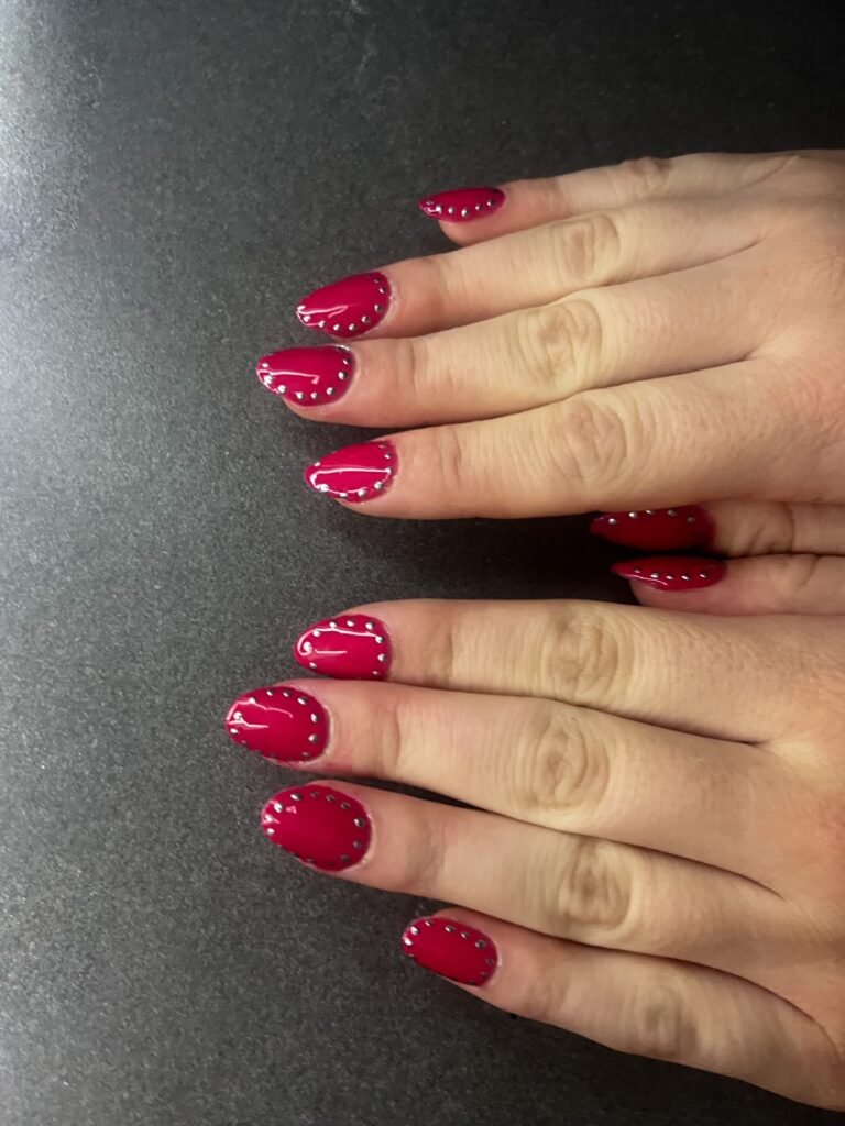 Short red nails ideas with rounded nails in deep red enhanced by silver bead accents lining the base of each nail.
