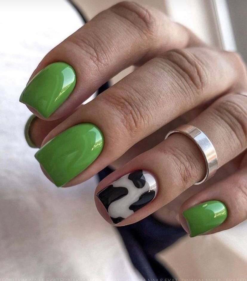 Short green nails ideas featuring glossy bright green polish with a fun cow print accent on one nail.