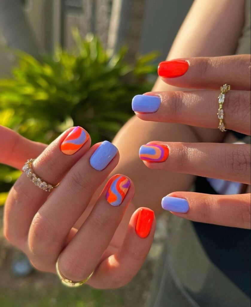 Hand displaying colorful short nail ideas for summer featuring retro swirl patterns in orange, blue, and purple hues with a natural green background.