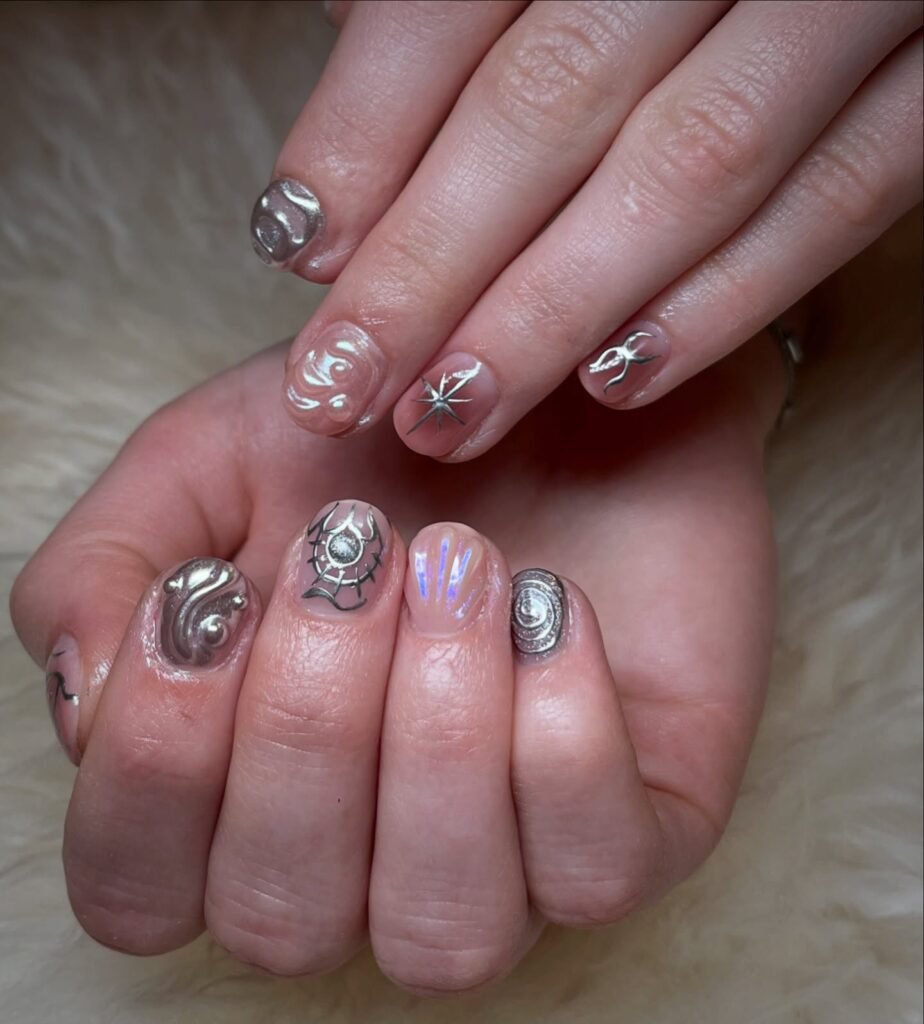 Unique very short nails ideas with ethereal silver designs including swirls, stars, flames, and spider webs on a translucent base.