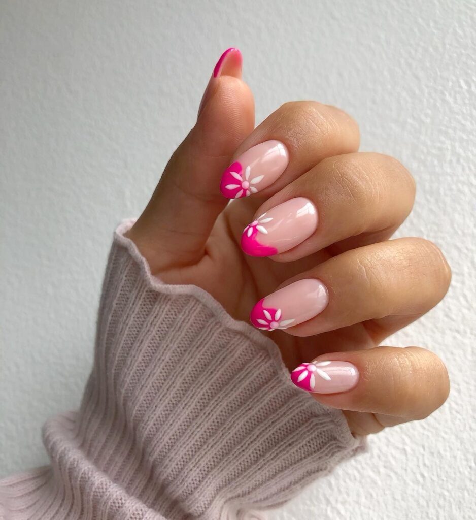 Cute barbie nails in pink with daisy flower designs on the French tips, shown on a hand against a neutral backdrop.