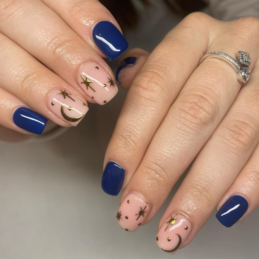 Stunning april nails ideas mixing navy blue polish with celestial gold star and moon designs on pink nails.
