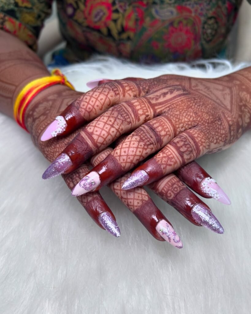 Beautiful engagement nails ideas indian with long stiletto nails in pink and purple glitter, adorned with rhinestones and paired with traditional henna designs.