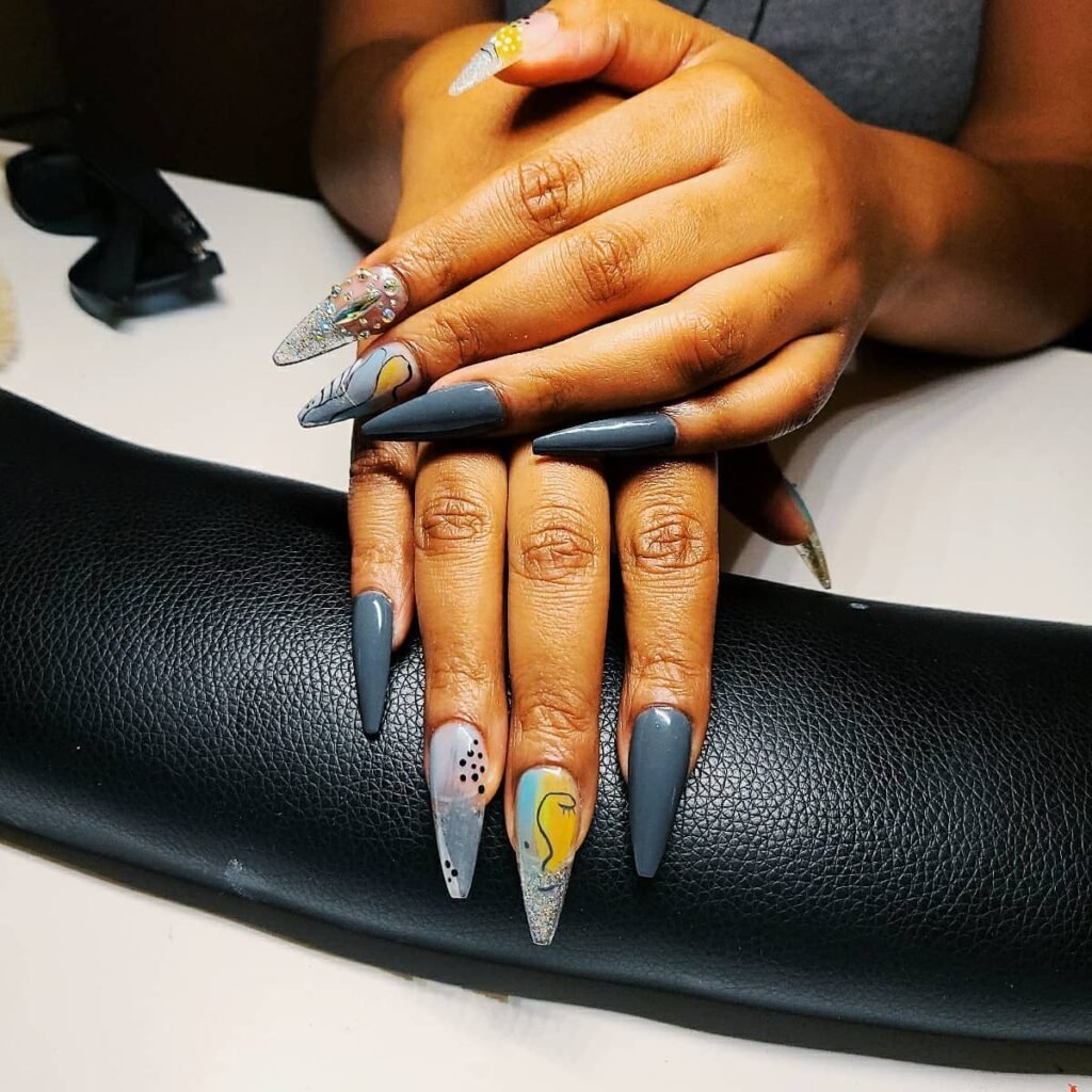 Creative grey nails ideas showcasing stiletto shapes with fun designs like smiley faces and rhinestones on a dark grey base.