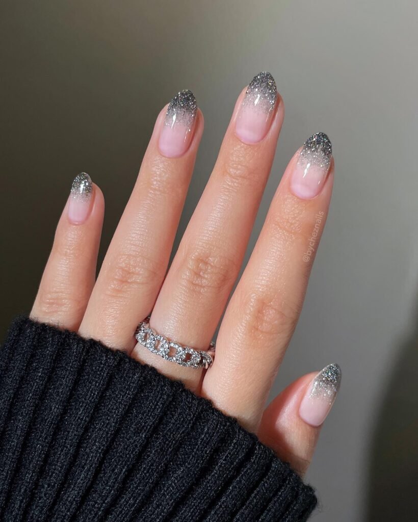 Sparkling grey nails ideas in ombre style blending nude bases with glittery grey tips on almond nails.