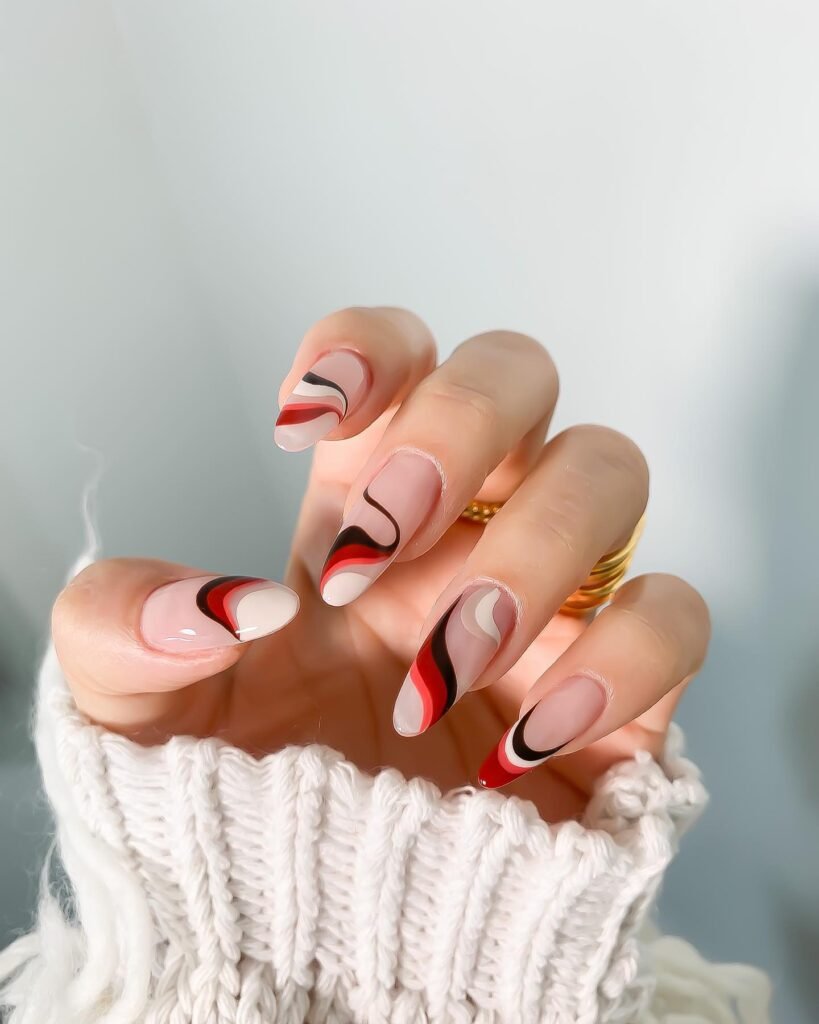 Close-up of hand showcasing creative May nails ideas with wavy abstract designs in red, black, and white on nude almond nails.