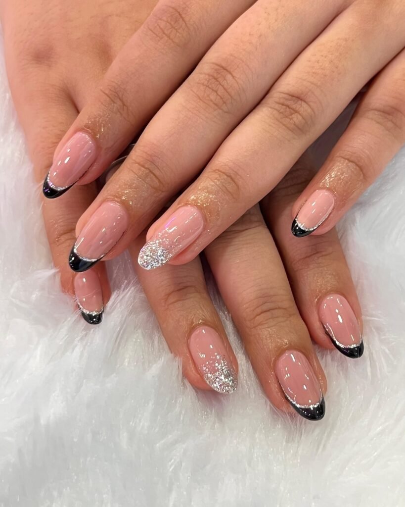 Hands displaying chic May nails ideas including nude bases with black French tips and subtle silver glitter accents.