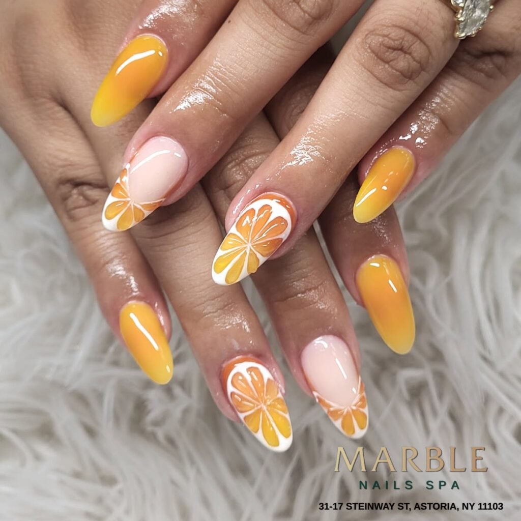 Hands presenting vibrant May nails ideas with orange ombré and cute citrus slice art on glossy almond nails.