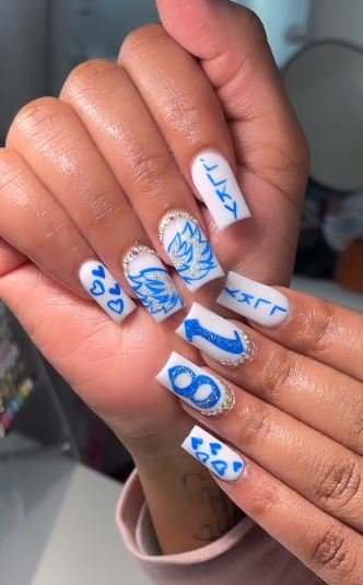 A close-up of a manicure featuring white nails with blue hearts, glittery numbers, and abstract designs, showcasing 18th birthday nails ideas.