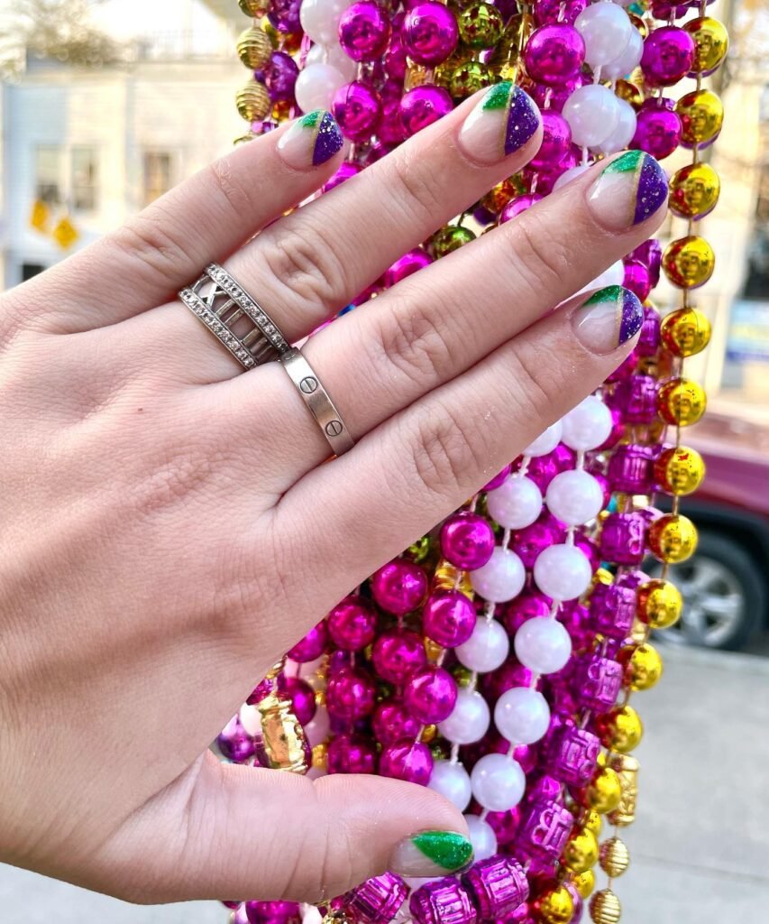 Purple green French tip nails held against colorful beads for creative Mardi Gras nails ideas