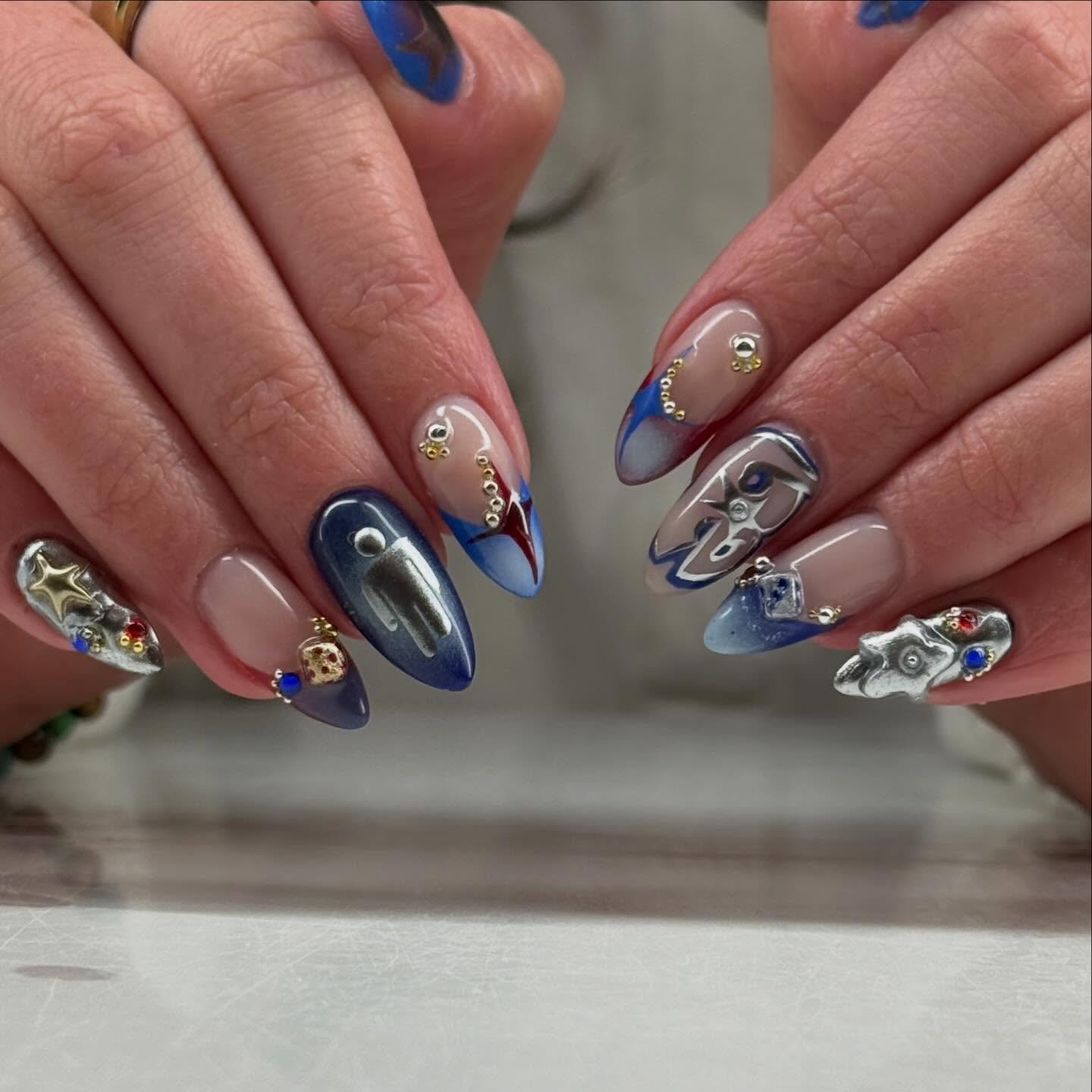 Creative blue chrome and red accent billie eilish nails ideas featuring 3D metallic skulls and star details on long almond nails