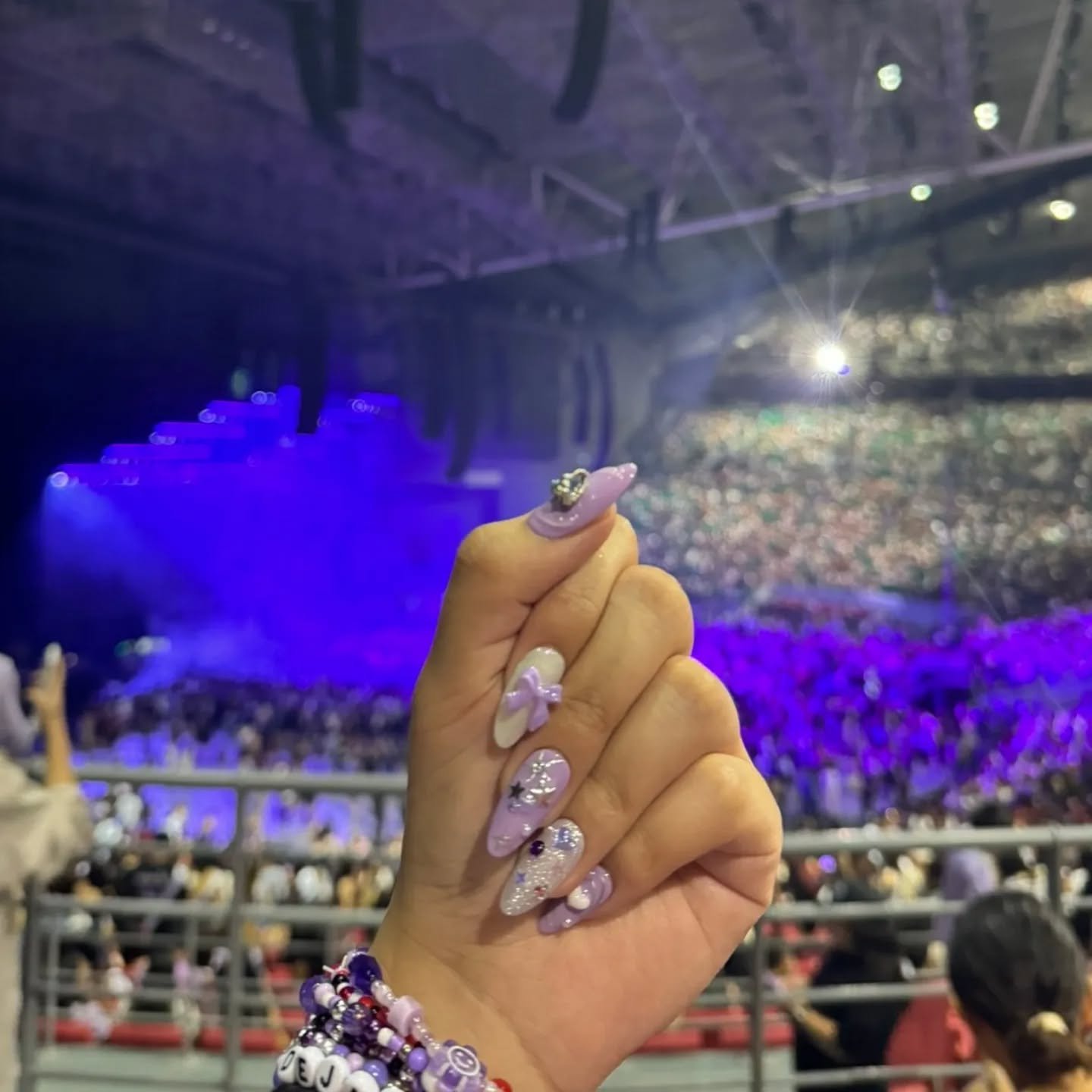 Elegant olivia rodrigo nails ideas showing purple glitter nails with bow and charm at a concert