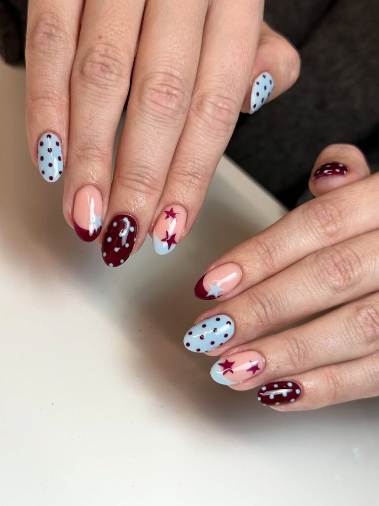 Hands showcasing elegant burgundy, peach and light blue nails with stars and polka dots as stylish nashville nails ideas