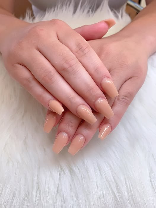 Long glossy beige nails resting on soft white fluffy background