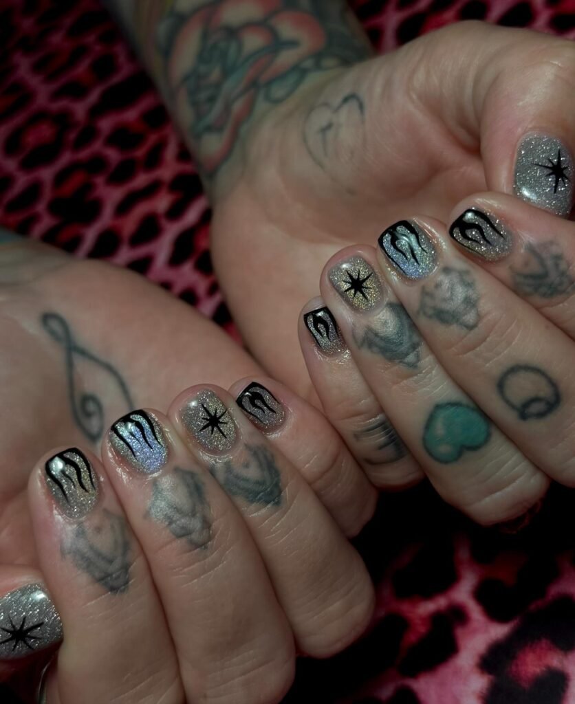 Discover these bold emo nails ideas in shimmering silver glitter with black star bursts, flame accents, and edgy tribal designs on tattooed hands