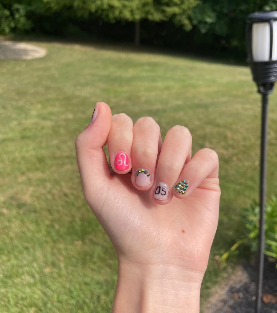Beautiful hand showing vibrant 18th birthday nails featuring bright pink, colorful rhinestones, and fun nail art
