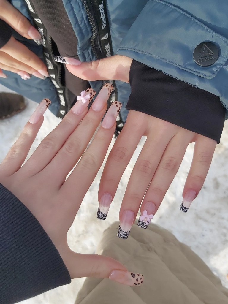 Trendy leopard, zebra, and bow best friend nails ideas with pink accents on long coffin nails in a snowy setting