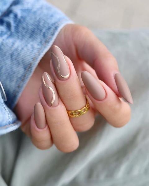 Modern beige nails featuring elegant gold wavy lines and gold ring