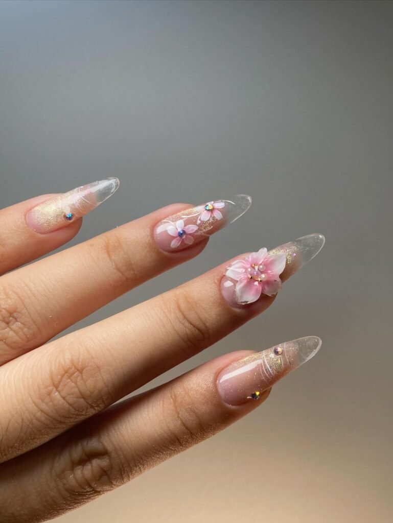 Luxurious clear nails ideas featuring 3D pink flowers, gold glitter, and crystal rhinestones on almond tips