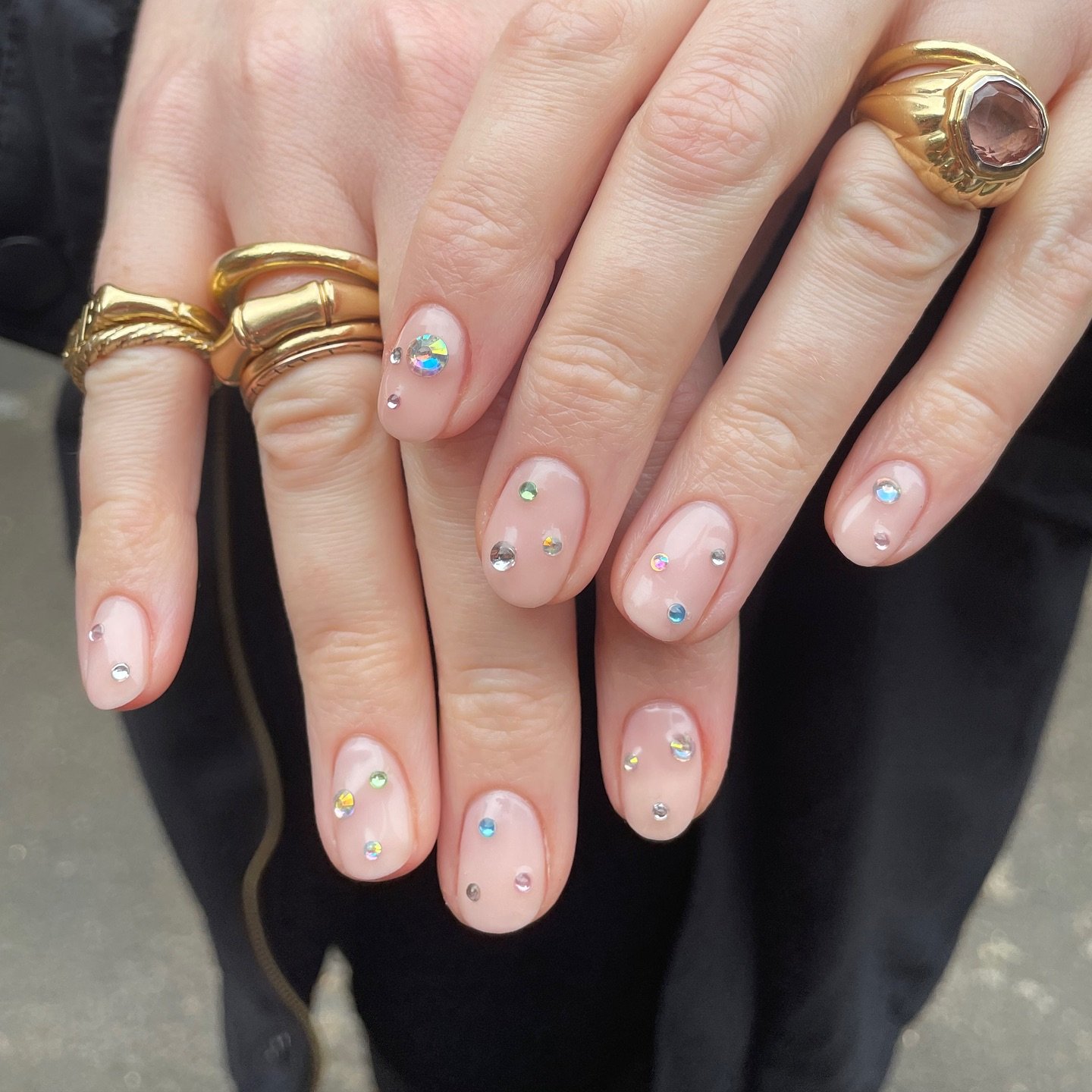 Delicate nude senior nails ideas adorned with tiny crystals and gold rings
