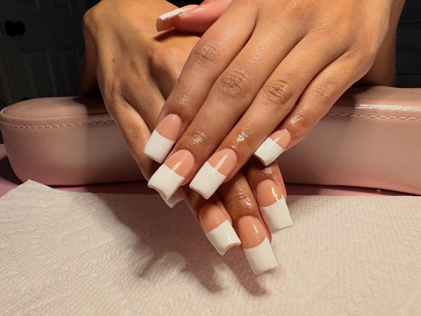 Hands resting on a pink manicure station displaying square nails with thick, crisp white tips over a peach base, perfectly capturing the bold, classic style of 2000s French tip nails.