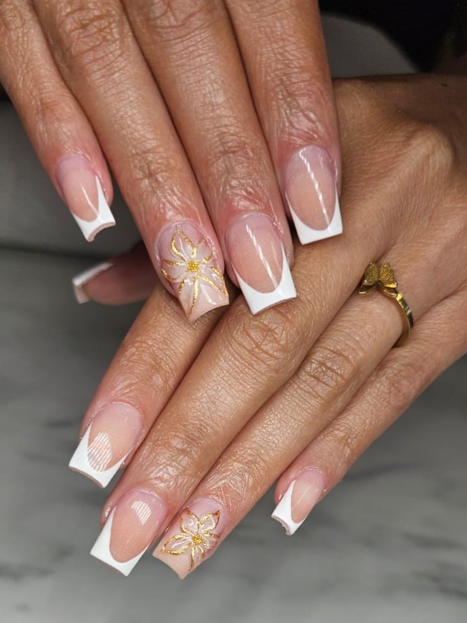 A close-up of two hands adorned with diamond rings resting near green succulents, featuring long, coffin-shaped natural french tip nails with a glossy nude base and crisp white edges.