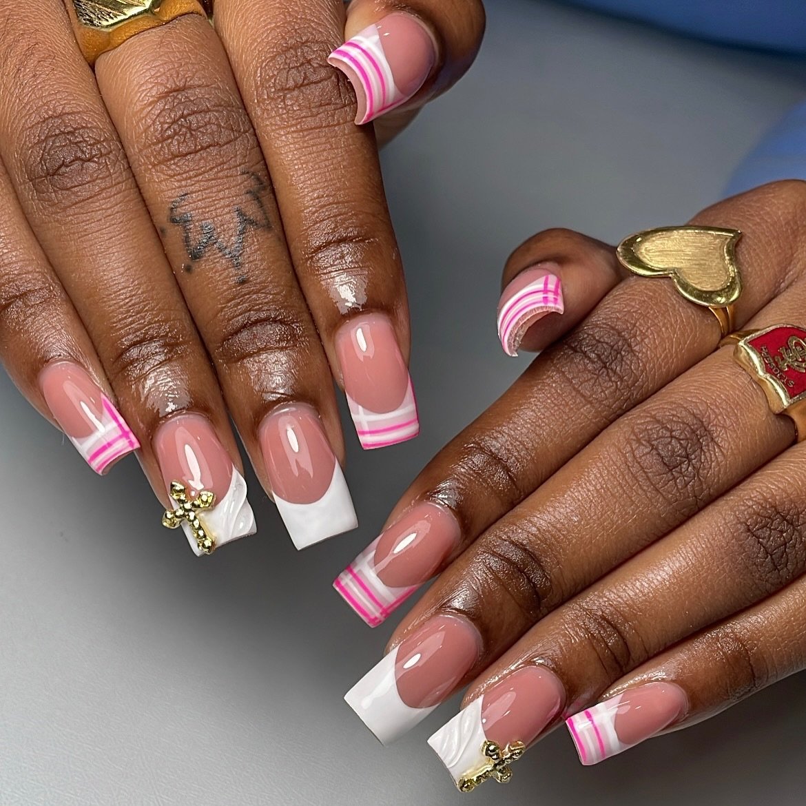 Long coffin-shaped nails featuring a mix of crisp white tips, pink striped accents, and gold cross charms, offering a bold and embellished take on 90s French Tip Nails.